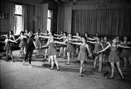 Czarno białe zdjęcie, na sali prób grupa młodych kobiet podczas ćwiczeń baletowych
