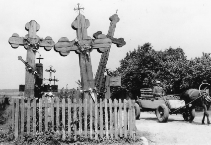 Drewniane krzyże przy drodze, w tle furmanka