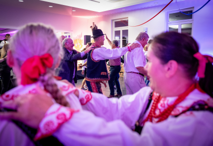 Goście na potańcówce oraz tancerze Regionalnego Zespołu "Podegrodzie" w strojach Lachów Sądeckich tańczą na Sali Kameralnej Centrum Folkloru Polskiego "Karolin". Ustawieni są "gęsio" i każdy trzyma się za ramiona osoby ustawionej przed nim.