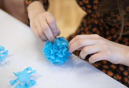 Uczestniczka warsztatów przywiązuje nitkę do dekoracji z niebieskiej bibuły