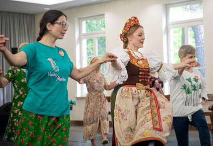Uczestnicy warsztatu i osoba prowadząca w kostiumie rozbarskim tańczą trojaka na Sali Kameralnej Centrum Folkloru Polskiego "Karolin"