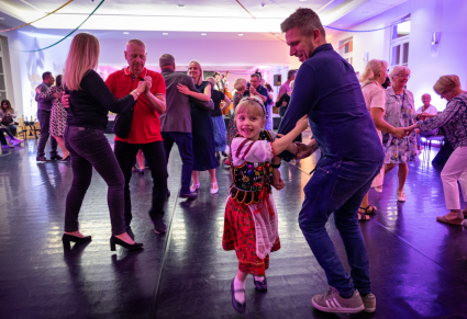 Sala Kameralna Centrum Folkloru Polskiego "Karolin" pełna tańczących gości. Na pierwszym planie dziewczynka w stroju krakowskim tańczy z tatą.