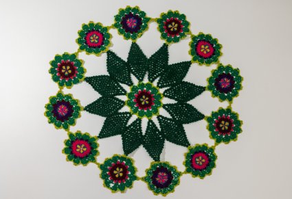 Okrągła serweta w dominującym kolorze zielonym z gwiazdą w środku i kwiatuszkami dookoła. Wykonana za pomocą koronki szydełkowej