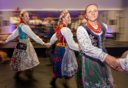 Uczestniczki potańcówki w strojach krakowskich tańczą "wężem", trzymając się za ręce