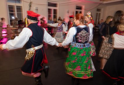 Uczestnicy potańcówki w strojach krakowskich tańczą w kręgu, ze złączonymi rękami