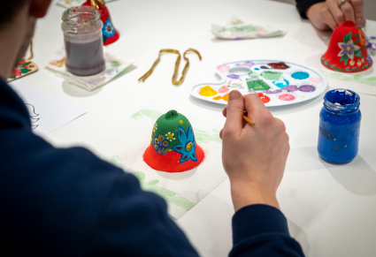 Uczestniczka warsztatów maluje dzwonek gliniany w kwieciste wzory