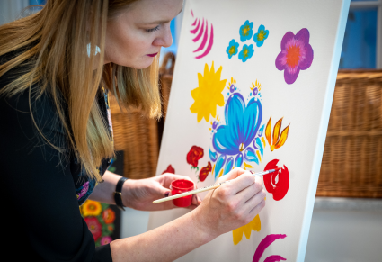 Uczestniczka warsztatów maluje kwiaty w stylu zalipiańskim na płótnie