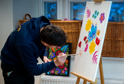 Uczestnik warsztatów maluje kwiaty w stylu zalipiańskim na płótnie