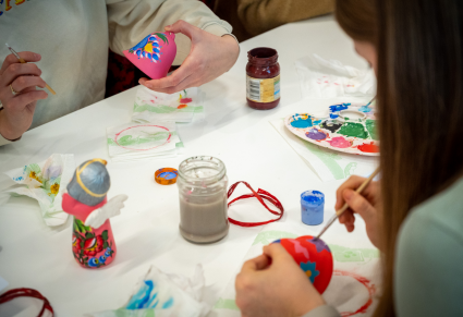 Uczestnicy warsztatów malują dzwonki gliniane w kwieciste wzory
