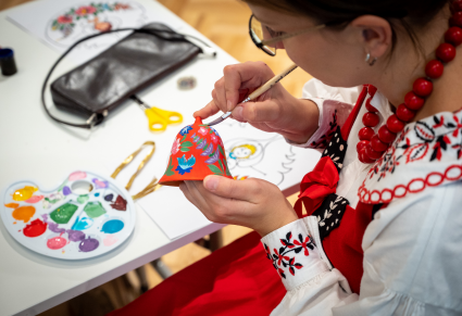 Osoba prowadząca warsztaty maluje dzwonek gliniany w kwieciste wzory