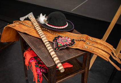 Elementy kostiumu podhalańskiego Zespołu "Mazowsze" - męski pas skórzany,  kapelusz, ciupaga, parzenica, kwiecista chusta - na drewnianym stoliku