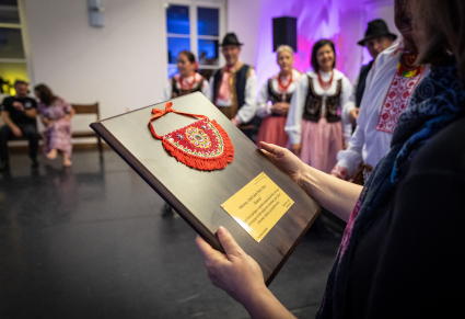 Kierowniczka Centrum Folkloru Polskiego "Karolin" trzyma w rękach pamiątkową tablicę z cioskiem podegrodzkim sprezentowaną przez członków Regionalnego Zespołu "Podegrodzie"