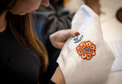 Uczestniczka warsztatów z haftu lachowskiego haftuje na płótnie kwiatek i liście