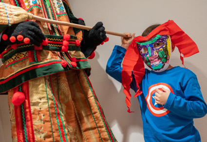Młody uczestnik warsztatu w samodzielnie wykonanej masce pozuje do zdjęcia przy manekinie ubranym w kostium śmiergustnika Zespołu "Mazowsze"