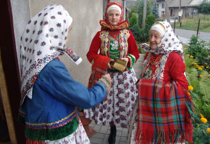 Kobiety w różnych rodzajach strojów wilamowskich, stojące przed wejściem do domu