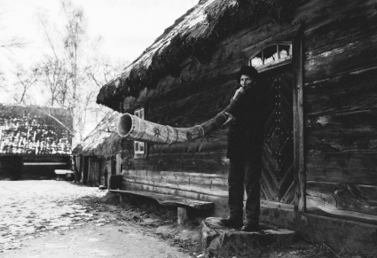 Mężczyzna grający na ligawce stojący przed drewnianym domem