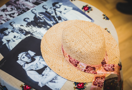 Słomiany kapelusz opasany malowaną wstążką leży na stole przy archiwalnych zdjęciach strojów śląskich