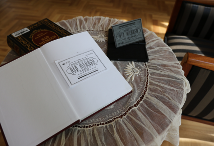 Książka "Nad Niemnem" leży na stole przy pieczątce przygotowanej na okazję Narodowego Czytania. Oparta na książce lektura, otwarta na pierwszej stronie, z kartką ostemplowaną pieczątką