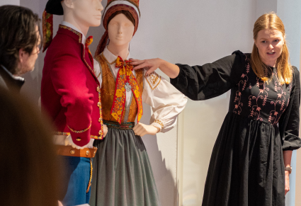 Pracowniczka Centrum Folkloru Polskiego "Karolin" pokazuje uczestnikom warsztatu kostium wilanowski Zespołu Mazowsze, w którym ubrane są manekiny na wystawie