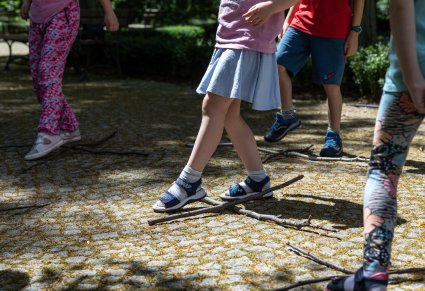 Zbliżenie na nogi dzieci, które przeskakują przez skrzyżowane patyki, ułożone na kostce na dworze, ćwiczą układ taneczny