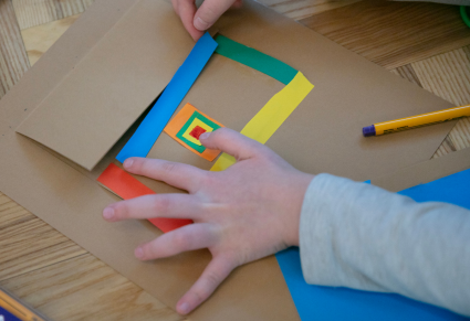 Zbliżenie: Dłonie dziecka układające kolorowe paski z papieru na brązowej kartce
