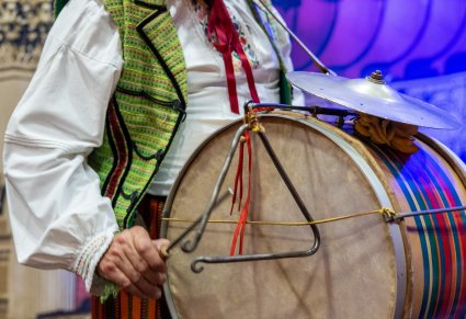 Zbliżenie na instrument – bęben ze stalką, który trzyma mężczyzna ubrany w kostium ludowy