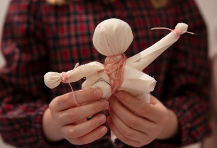 Ręce kobiety, trzymające niedokończoną lalkę, głowa i ręce ukształtowane z jasnego materiału.