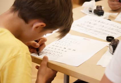 Młody chłopiec w skupieni pisze po kartce piórem