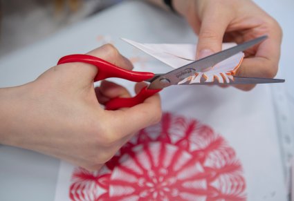 Zbliżenie na dłonie, które trzymają nożyczki i nacinają wzory w zgiętym papierze
