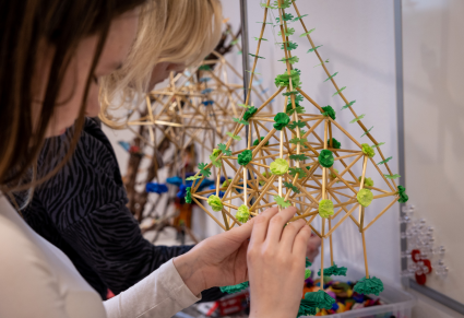 Uczestniczka warsztatów zdobi słomianą konstrukcje - pająka - zielonymi dekoracjami z papieru i bibuły