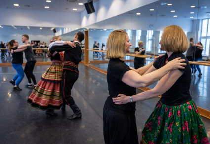 Pary  tancerzy objętych w "okrągłym" trzymaniu tańczą na sali prób PZLPiT 'Mazowsze". Osoby prowadzące tańczą w kostiumie krzczonowskim.