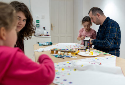 Uczestnicy warsztatów malują chusty we wzory kwieciste i dekorują je błyskotkami, przy wsparciu rodziców