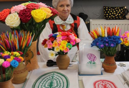 Rękodzielniczka kurpiowska siedzi przy stoisku z wycinankami i kwiatami z bibuły