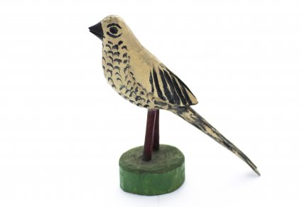 Drewniana figurka beżowego ptaka, ptak na brzuchu i ogonie ma czarne pióra. Umieszczony jest na drewnianym patyku