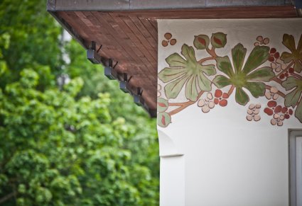 Fragment elewacji, namalowane liście oraz kwiaty kasztanowca znajdują się na ścianie pod dachem