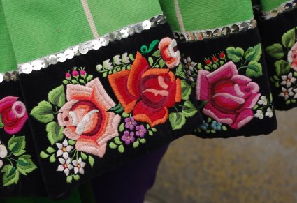 Zbliżenie na fragment łowickiej spódnicy, na dolnej części na aksamici wyhaftowany wzór łowickich, kolorowych kwiatów