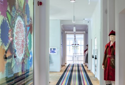Korytarz w Pałacu Karolin, na podłodze pasiasty dywan, po lewej kolorowa szyba, po prawej manekin w ubraniu kosyniera
