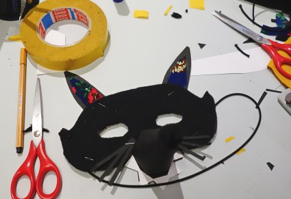 Czarna maska kota z kolorowymi uszami leży na stole warsztatowym