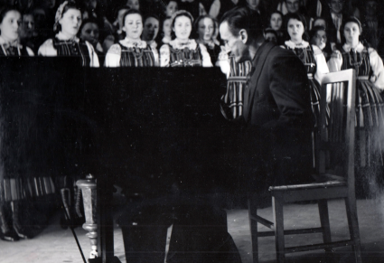 Przy fortepianie siedzi Tadeusz Sygietyński w tle stoi chór Zespołu