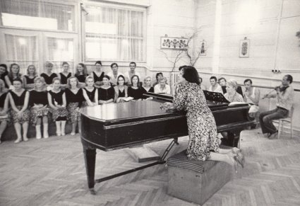 Mira Zimińska-Sygietyńska opiera się o fortepian, w sali prób, zespół w rzędach siedzi pod oknem