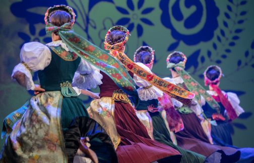 Mazowsze Ensemble dancers on stage in costumes from Rozbark, with decorative ribbons attached to their headdresses
