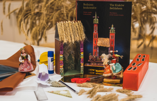 Materiały do przygotowania szopki leżące na stole, w tle książka dotycząca dziejów krakowskich szopek