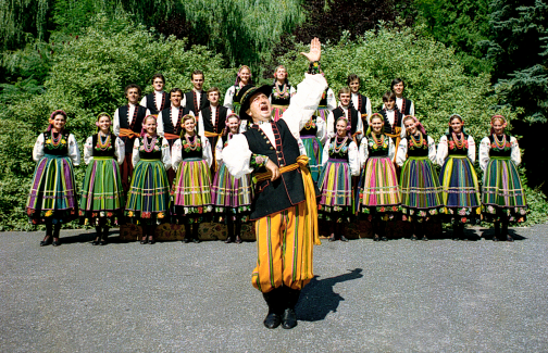 Chór w kostiumach łowickich, na pierwszym planie śpiewający solista z uniesioną do góry lewą ręką