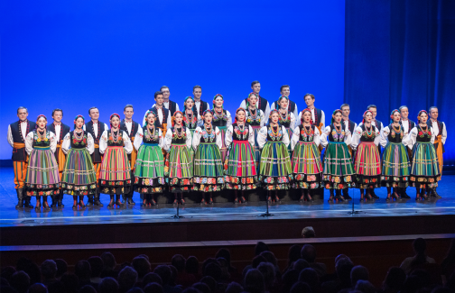 Mazowsze Ensemble choir on stage in costumes from the region of Kocierzew.  The women are standing in a row in front of the men.