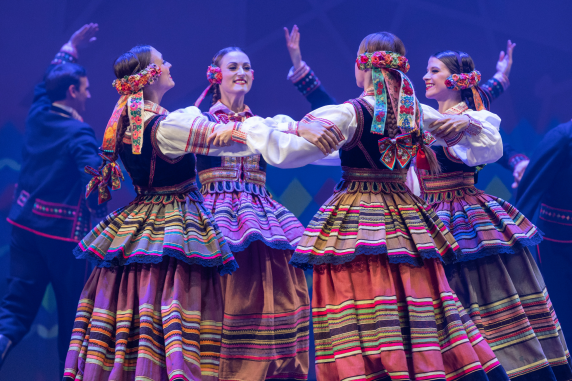 Cztery dziewczyny tańczące w kole w kostiumach krzczonowskich, w tle tancerze