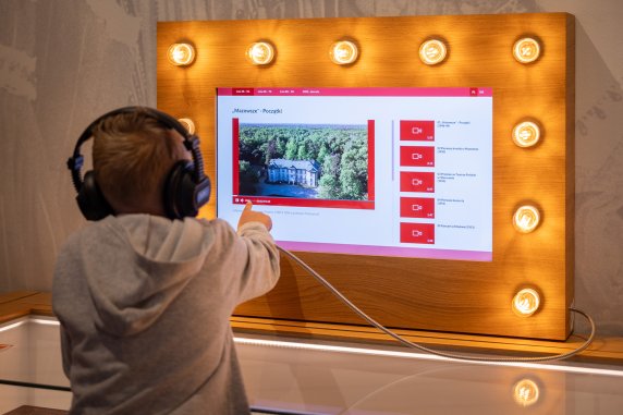 Dziecko ze słuchawkami przy ekranie na wystawie Centrum Folkloru Polskiego "Karolin"