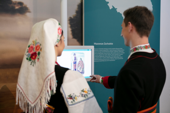 A couple in Polish folk costume look at photographs on a screen in the Centre for Polish Folklore