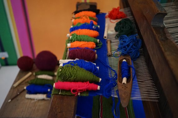 Warsztat tkacki, drewniane krosno, na nim leżą kolorowe nici