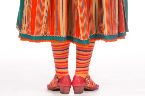 Fragment kostiumu wilamowskiego, pokazane nogi do kolan, pantofle, pasiaste pończochy i fragment spódnicy