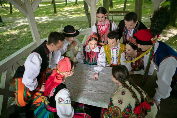 A group of young people in folk costumes sitting in a gazebo and studying a map